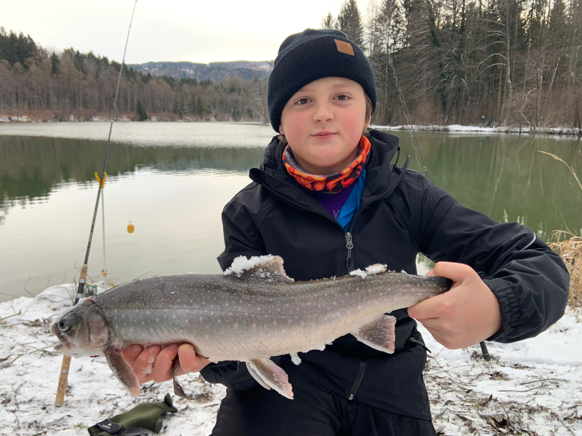 Junger Fischer mit einem Saibling im Winter am Gewässer